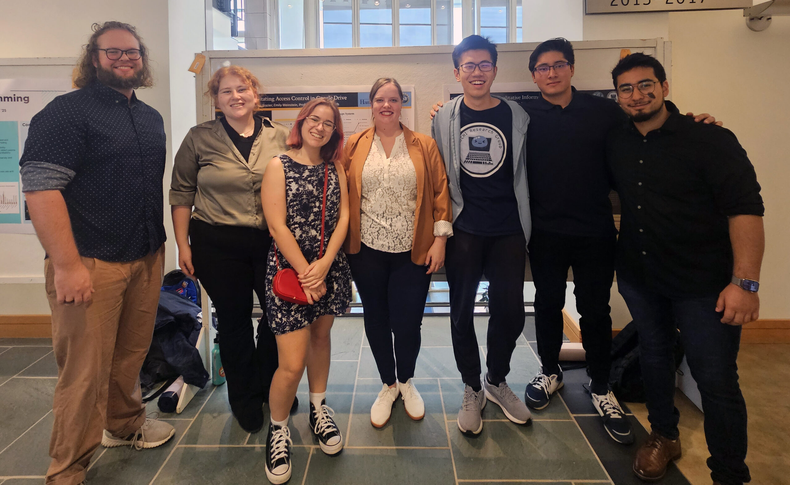 The MoCHI Research Lab stands in front of their posters at family weekend on Hamilton's campus in 2023. From left to right, James Frazier, Emily Weinstein, Iris Izydorczak, Sarah Morrison-Smith, Ivan Wu, Matthew Maillet, and Sebastian Favela