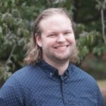 James Frazier poses outdoors while wearing a blue button down shirt