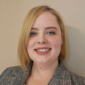 rof. Morrison-Smith poses wearing a grey blazer in front of a beige wall.