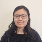 Catherine poses in front of a beige wall wearing a black shirt and hoodie.