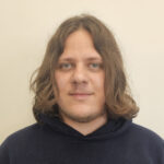 Seth poses in front of a beige background while wearing a navy hamilton hoodie.