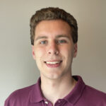 Ethan poses in front of a beige background while wearing a maroon polo shirt