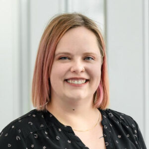 Sarah Morrison-Smith is a white woman with blonde and pink hair wearing a black button down shirt